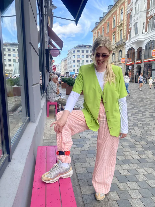 A cyclist in pink trousers with a strap at the ankle, one foot up on a pink bench
