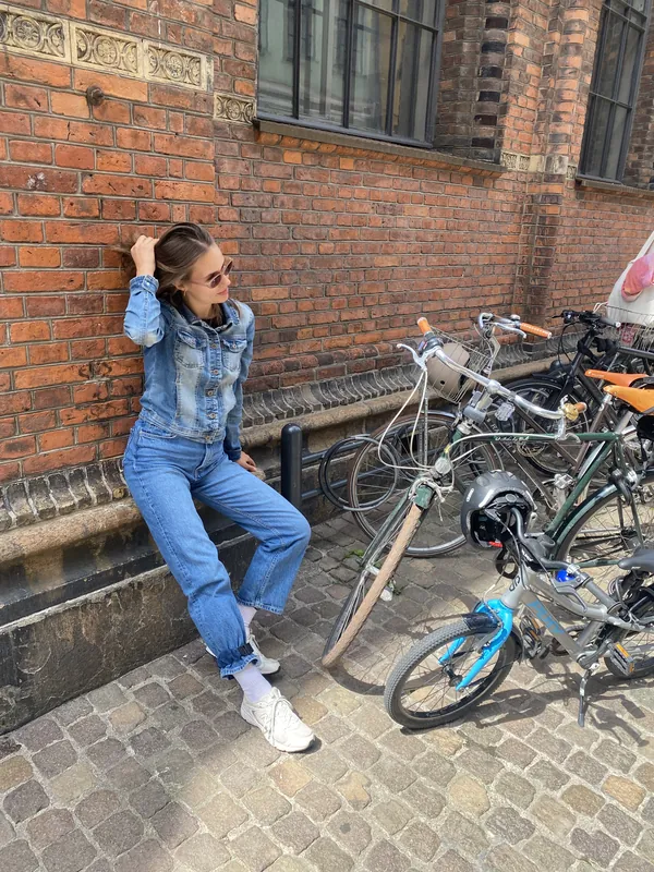 A rider in double denim sitting by a brick wall next to parked bikes