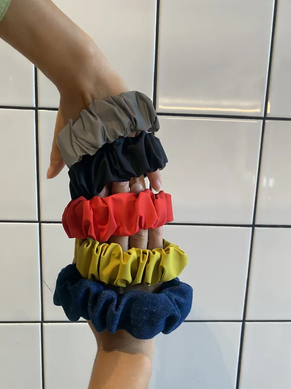 A hand wearing five straps stacked like bracelets against white tiles