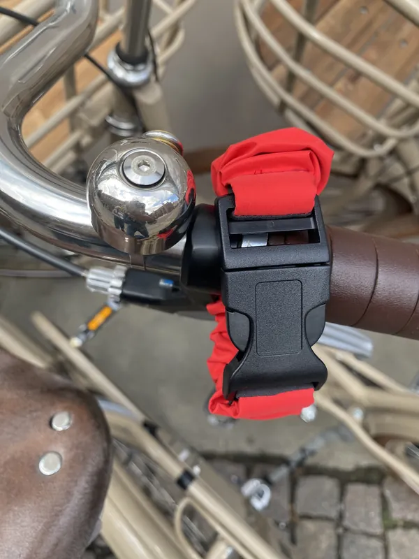 A Coral Red strap clipped to a bike handlebar beside the bell